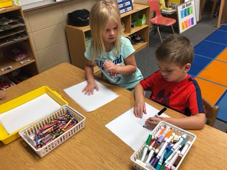 Two children drawing at a table in a classroom