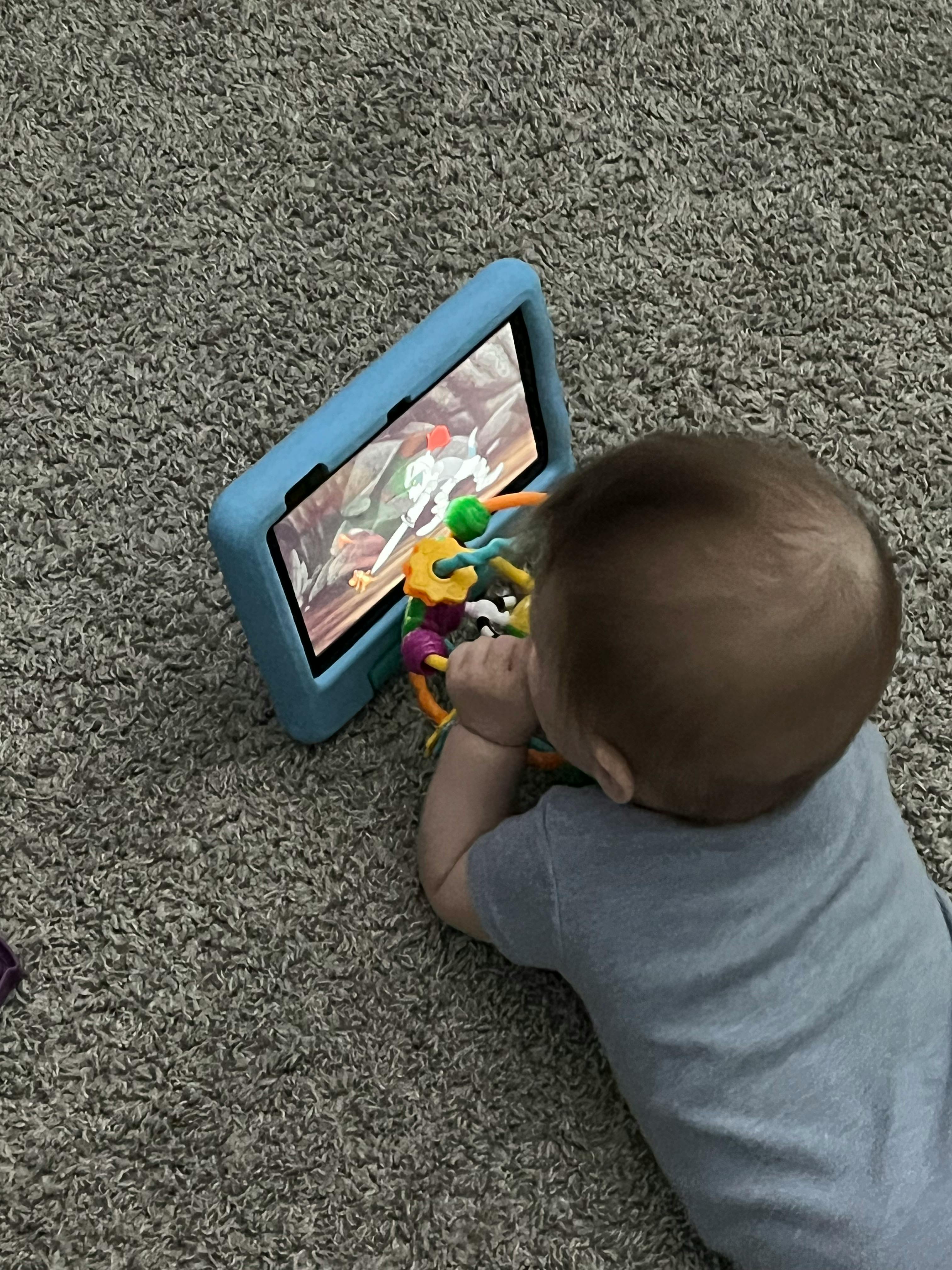 Child on carpet looking at a tablet with a toy
