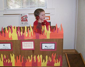 Child in a cardboard box decorated to look like a burning building