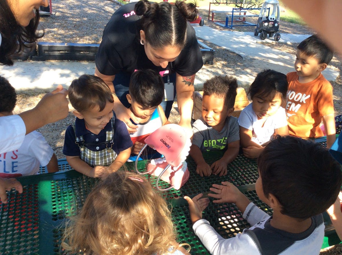 Person showing a pink object to a group of children around a table
