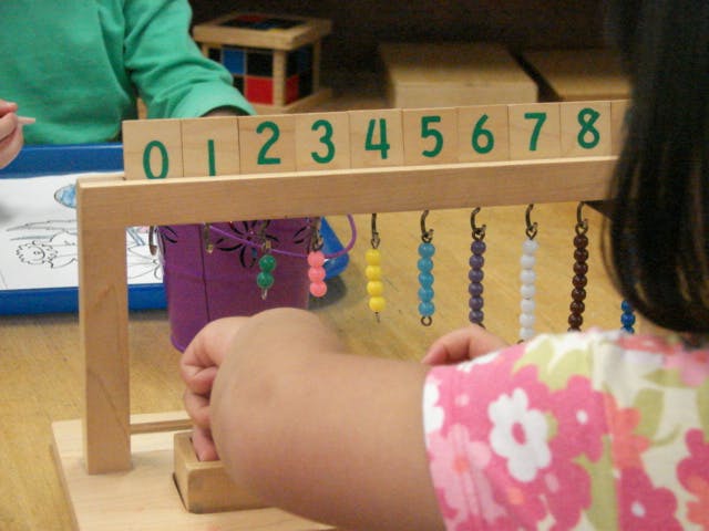 Child using a wooden counting frame with numbered blocks and beads
