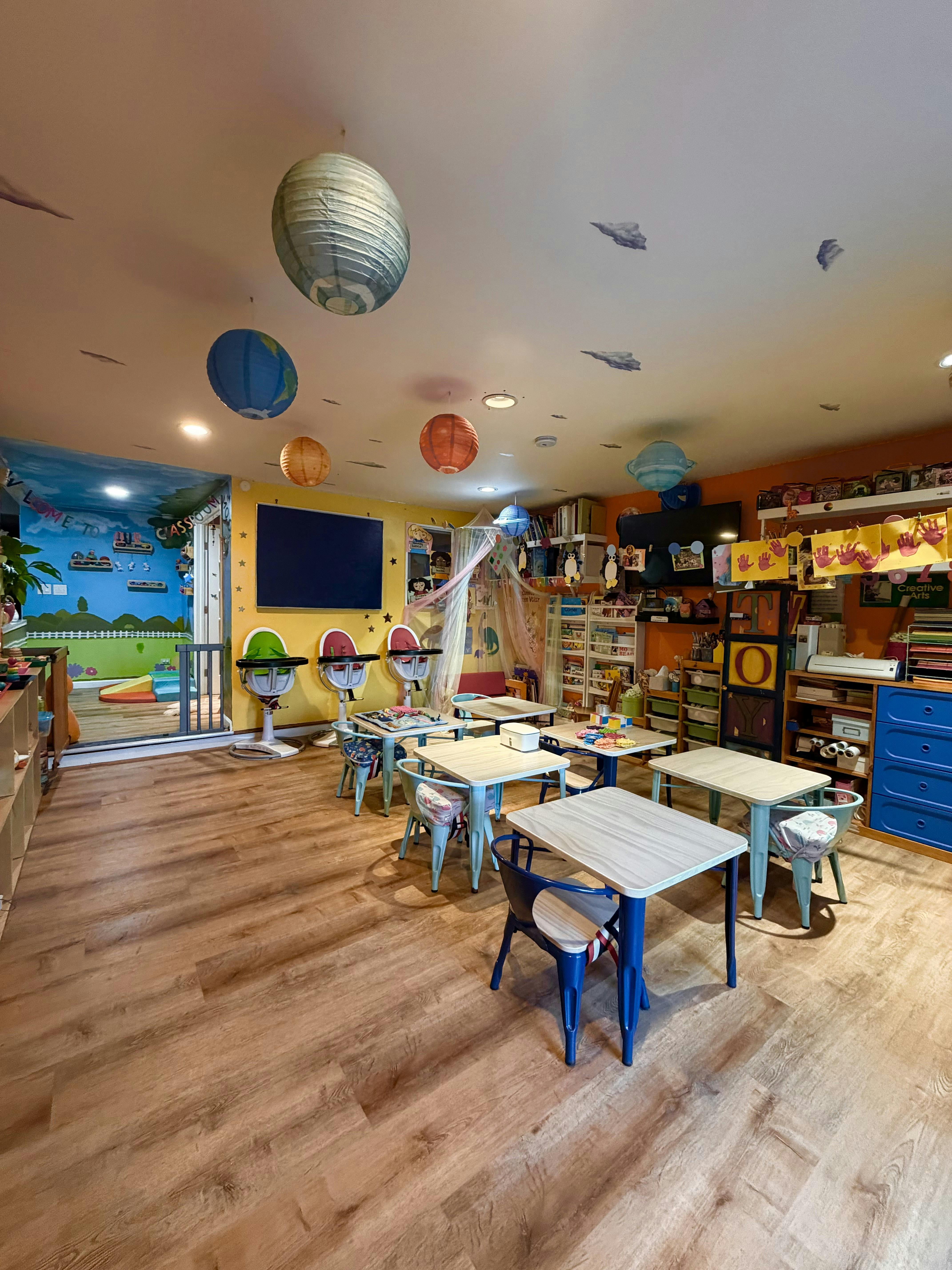 A classroom with small tables and chairs, two high chairs, and planet-themed decorations