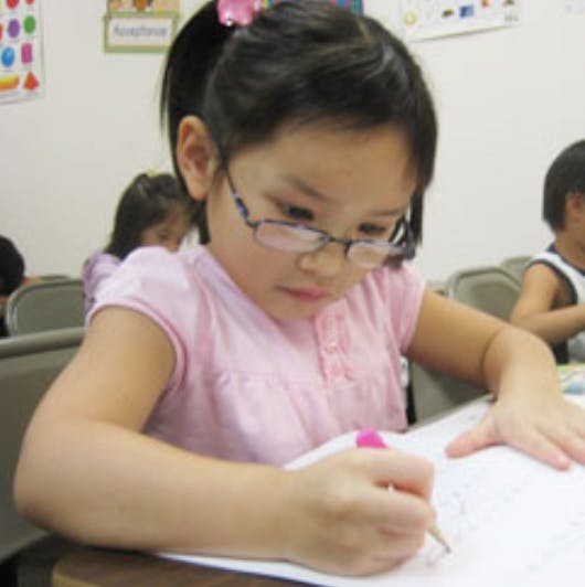 Child in glasses writing on paper in a classroom