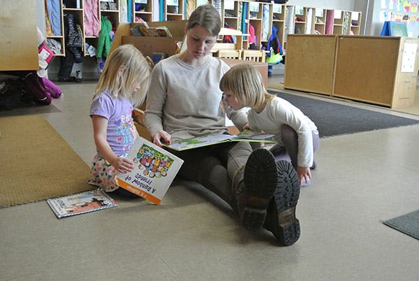 Person sitting on floor reading book with two children