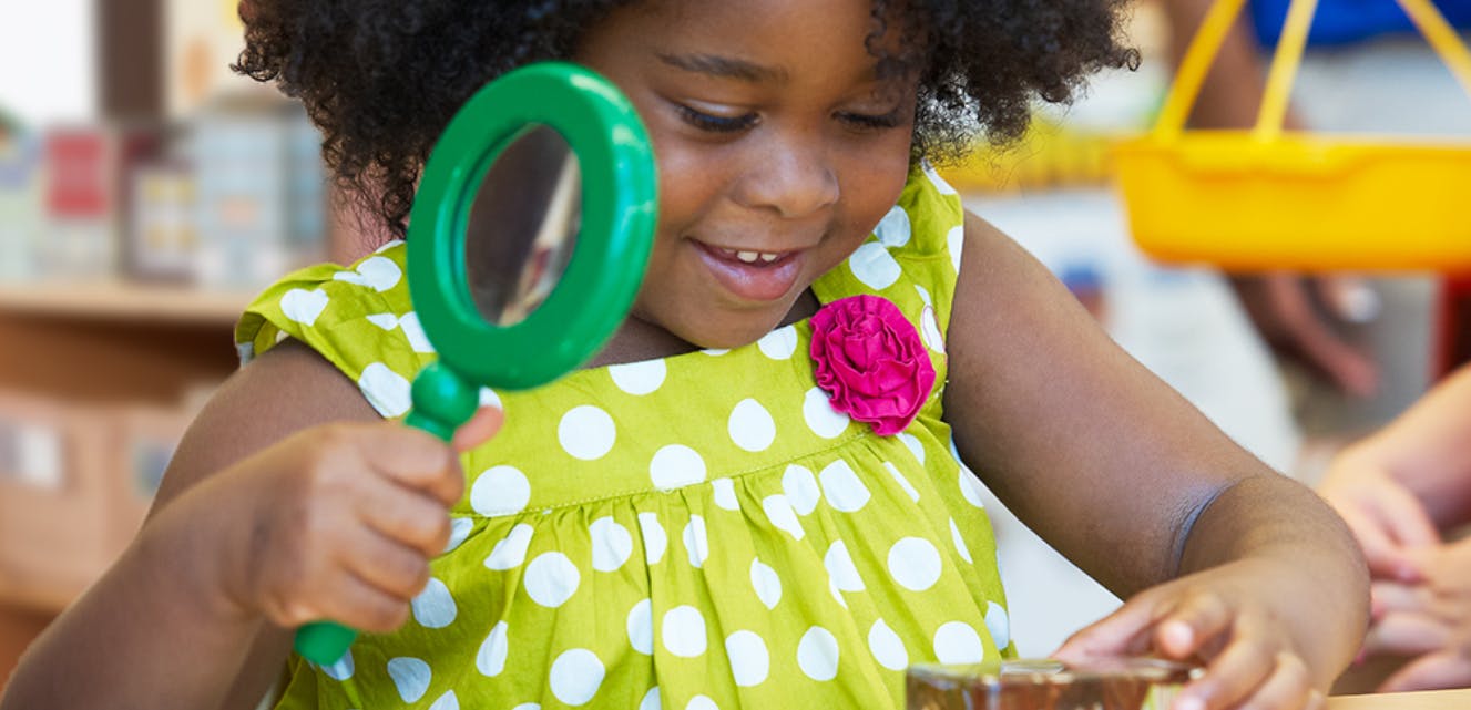 Child holding a magnifying glass over an object