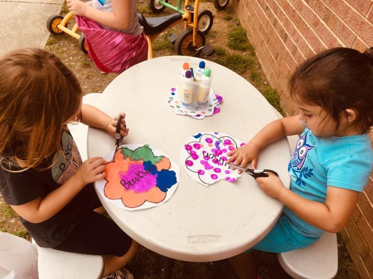 Two children doing crafts at a small table outdoors