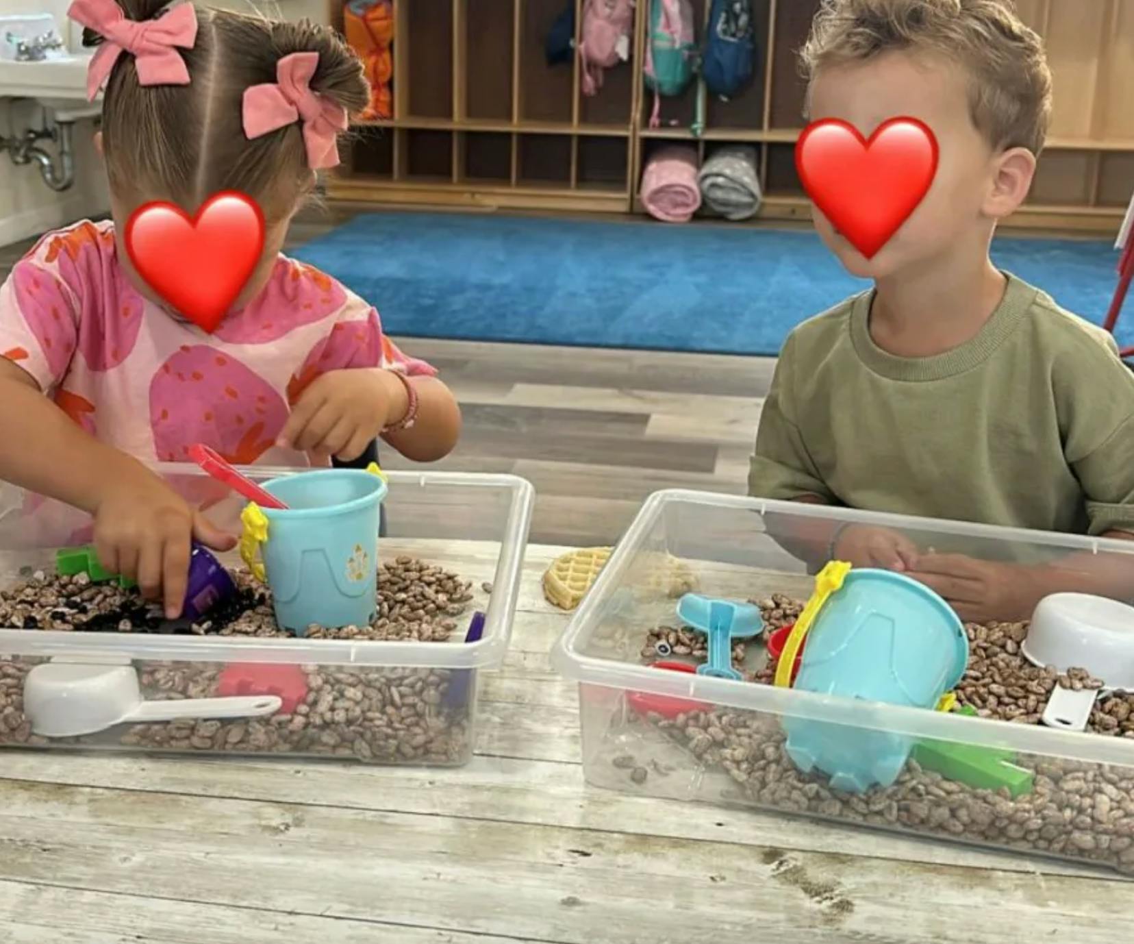 Two children playing with plastic buckets and beans in sensory bins