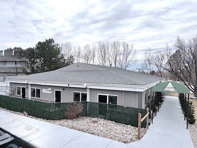 An exterior view of a gray building with a green awning over a walkway