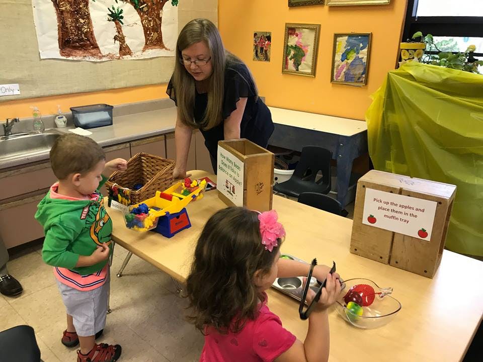Adult supervising two children playing with toys at a table