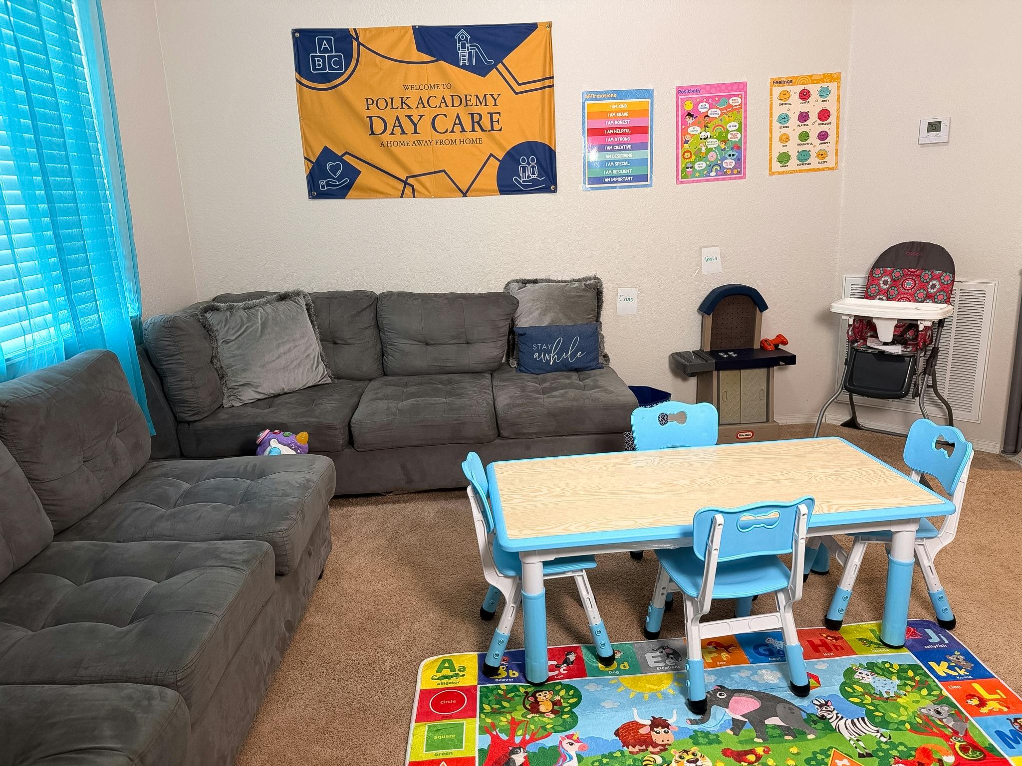 Living room with two gray couches, a child-sized table with blue chairs, and a playmat