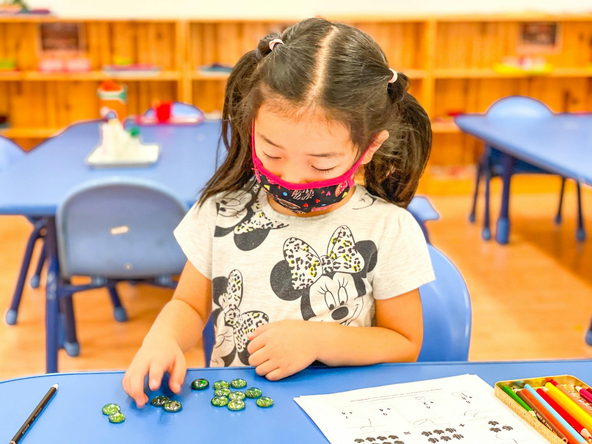 Child in a mask doing an activity at a table in a classroom