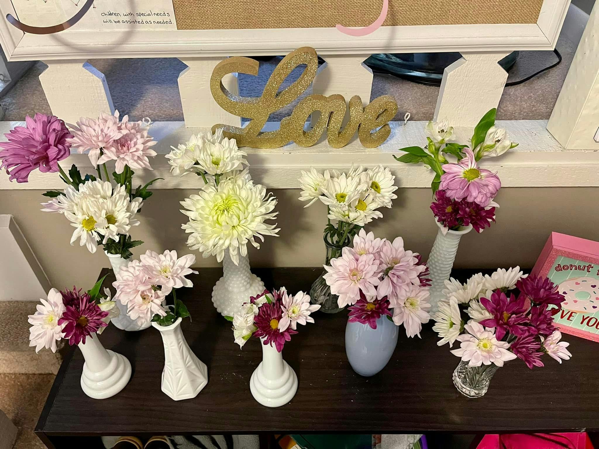 multiple small bouquets of flowers in various vases with a glittery "Love" sign