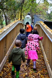 Adult and children walking on a bridge covered in leaves