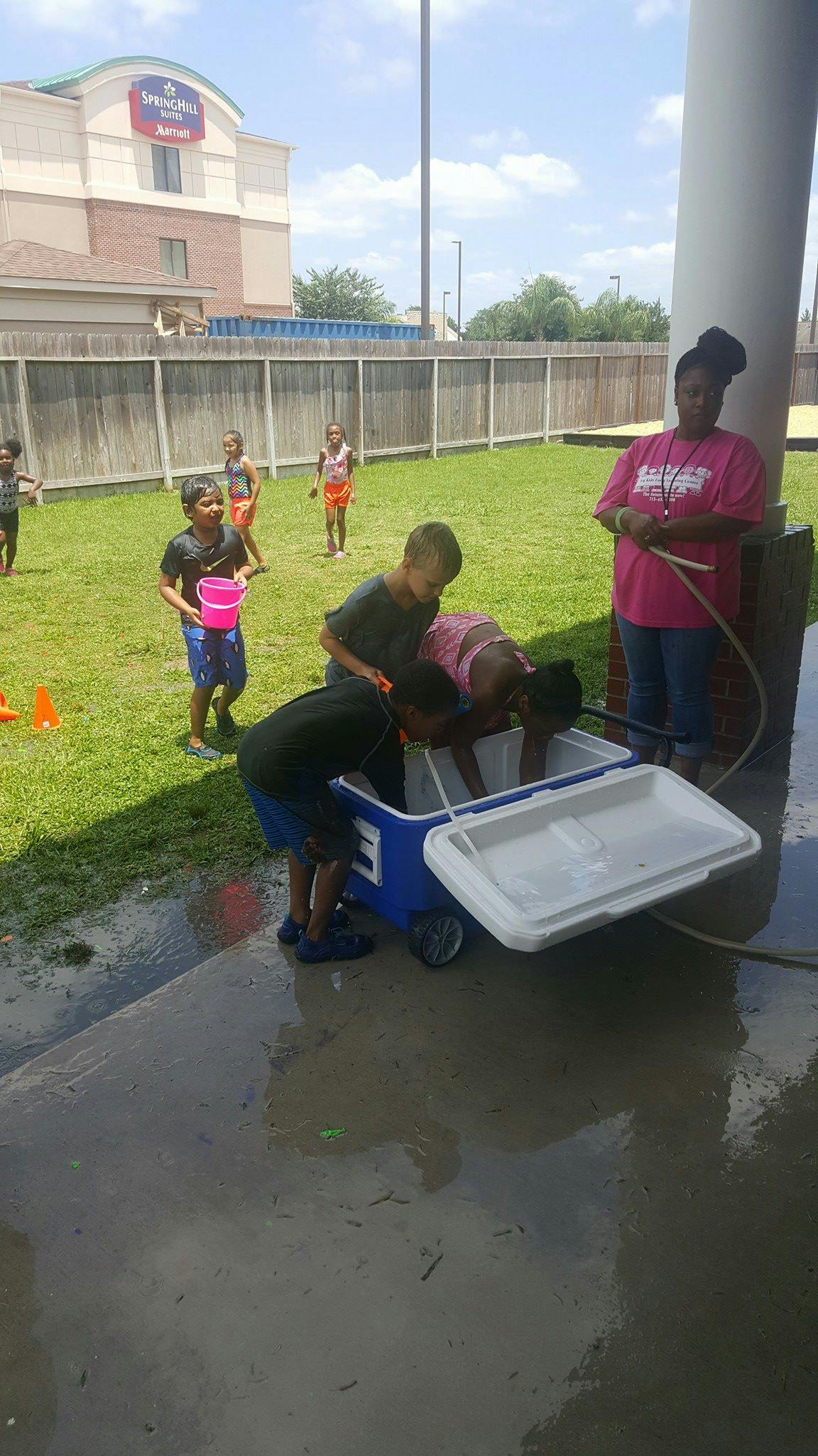Children playing with water from a cooler outdoors, with an adult nearby