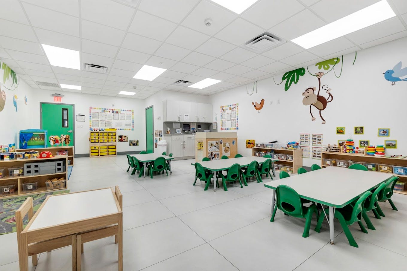 Classroom with small tables and chairs, shelves with toys, and wall murals