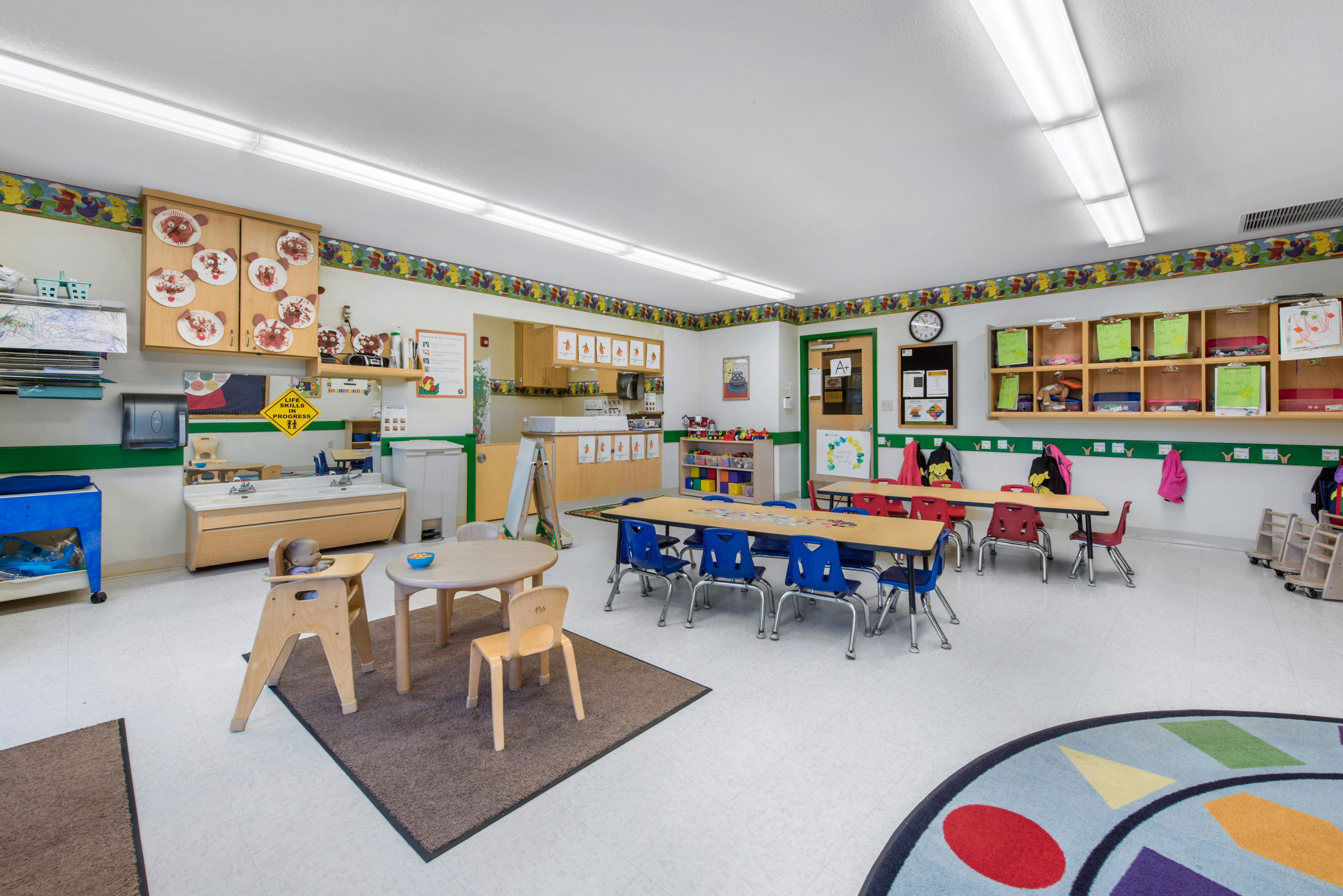 Classroom with small tables, chairs, two sinks, and a baby doll in a high chair