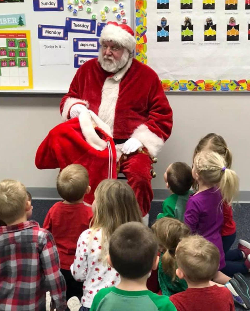 Person in red suit and white beard sitting with children gathered around