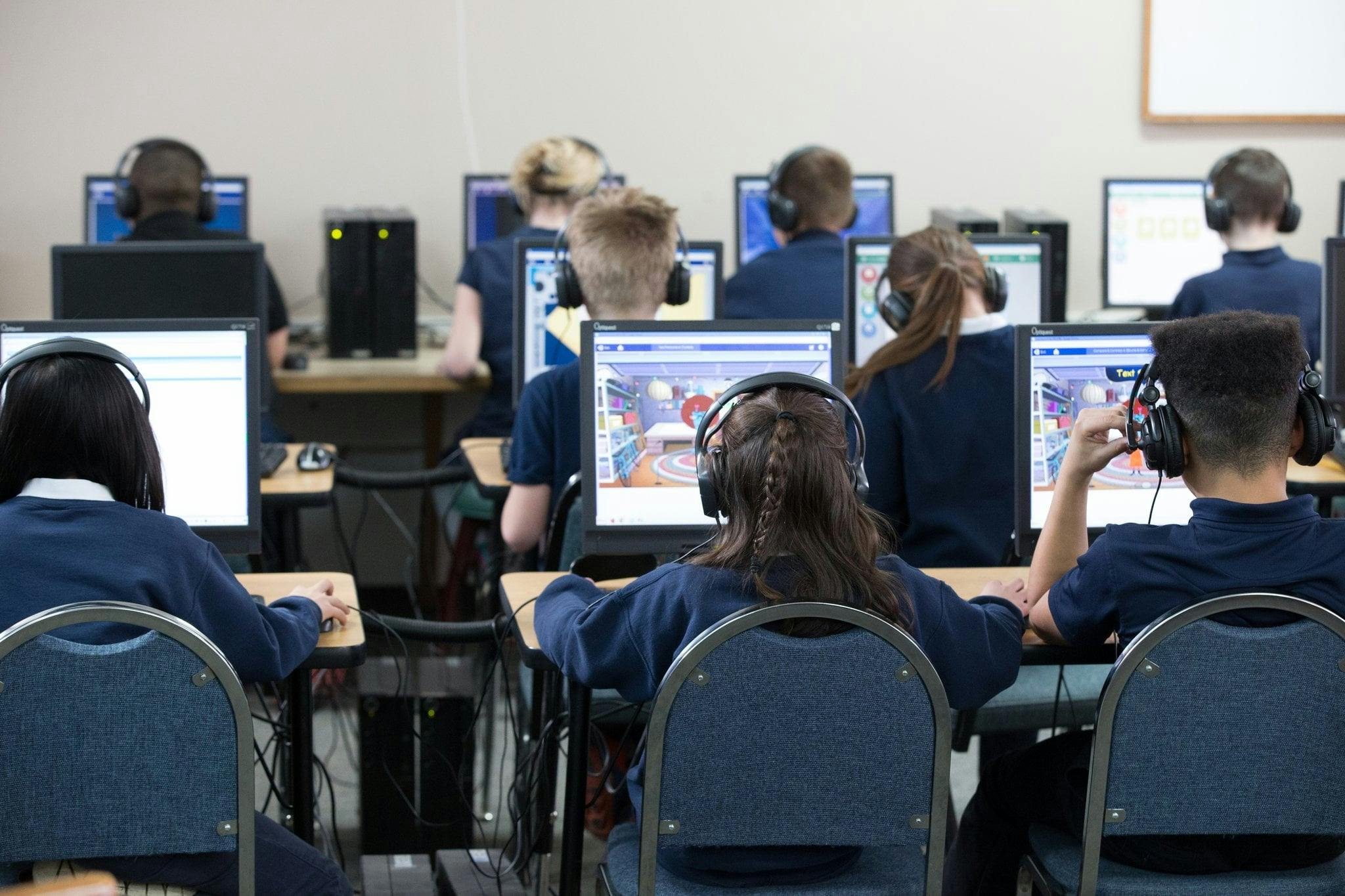 Students in a computer lab with headphones on, facing their monitors