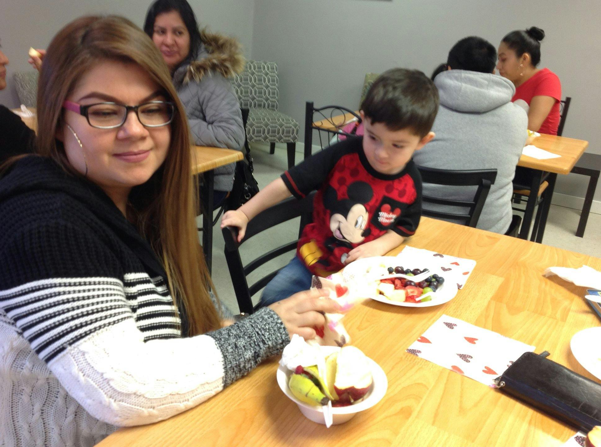 Person decorating a dessert with a child sitting at a table