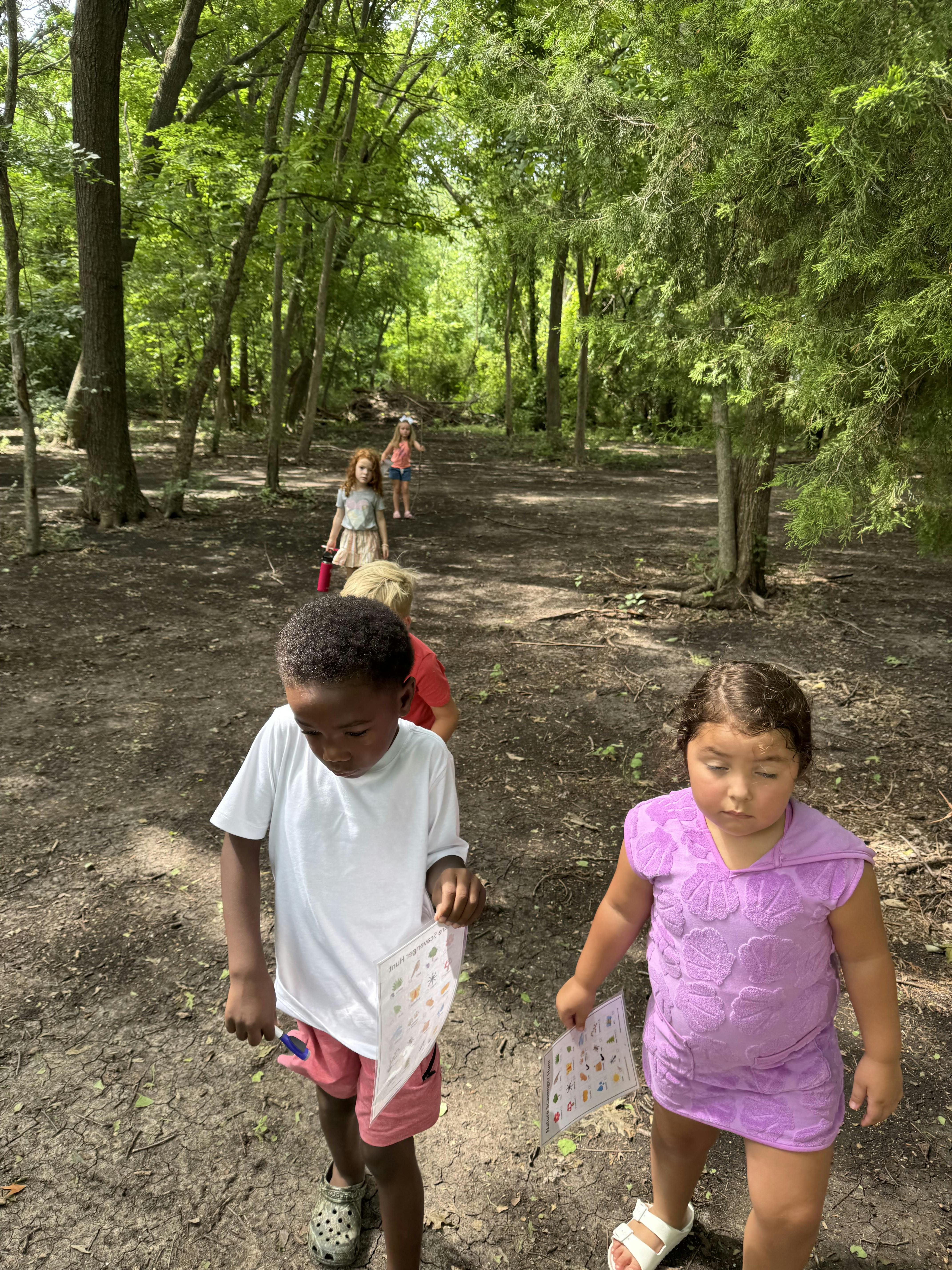 Children walking on a dirt path in a wooded area