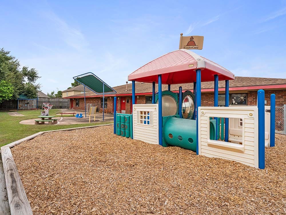 Playground structure with a red roof, tunnel, and a KinderCare flag