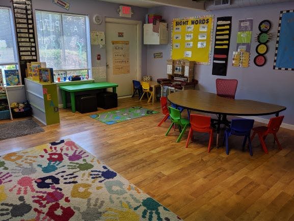 Classroom with small tables and chairs, colorful rugs, and educational posters