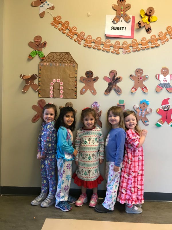 Five children standing in pajamas in front of a wall decorated with gingerbread people
