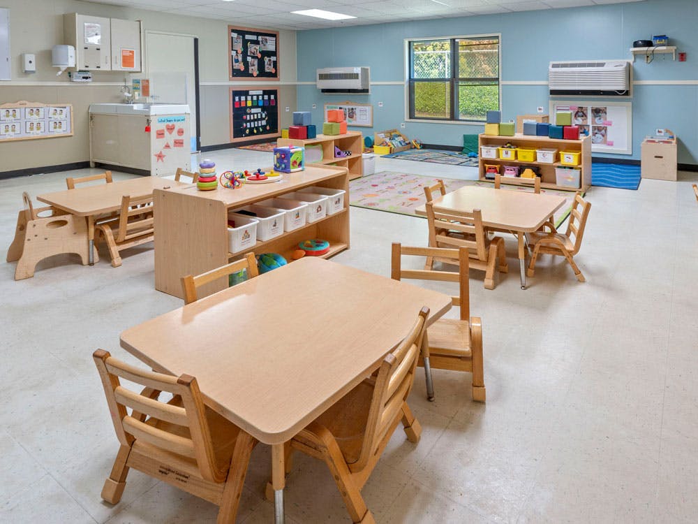 Classroom with small wooden tables and chairs, toys on shelves