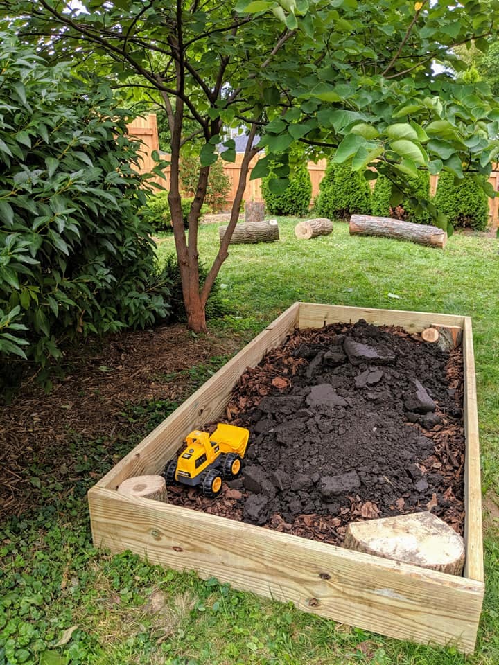 Yellow toy dump truck in a wooden sandbox filled with dirt