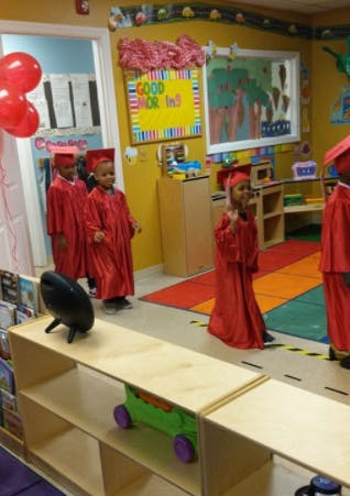 Children in red graduation gowns and caps in a classroom