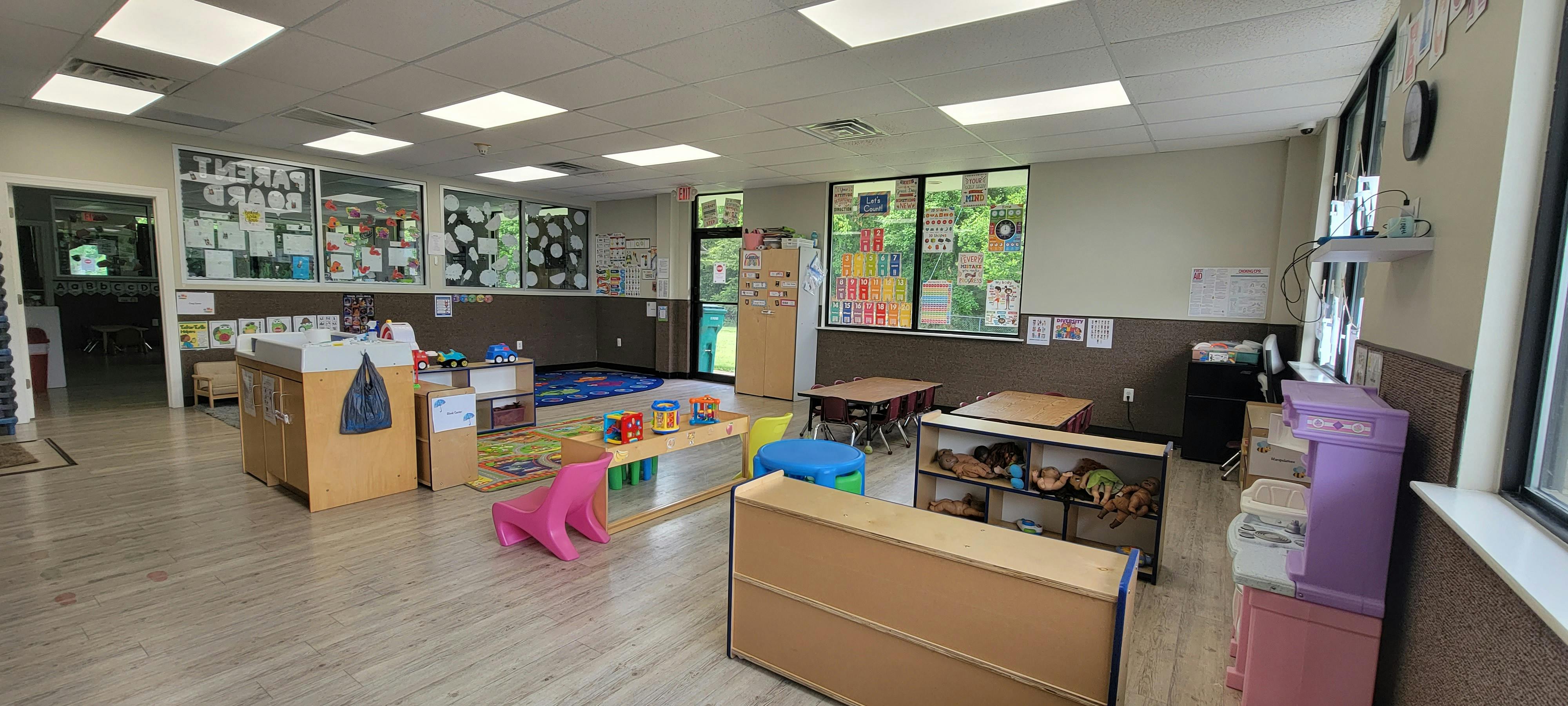 A colorful empty classroom with small tables, chairs, toys, and educational posters