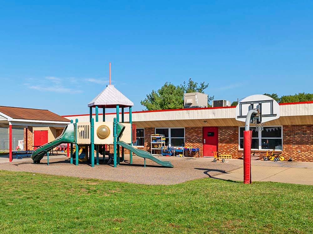 Playground with slides next to a brick building and a basketball hoop