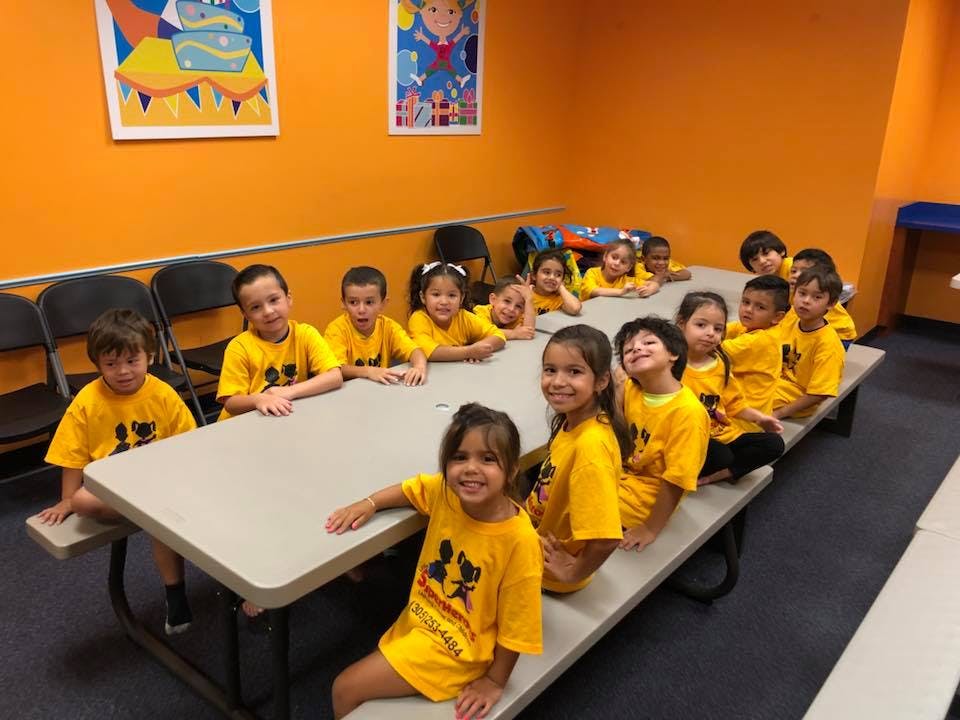 Group of children in yellow shirts sitting at a long table