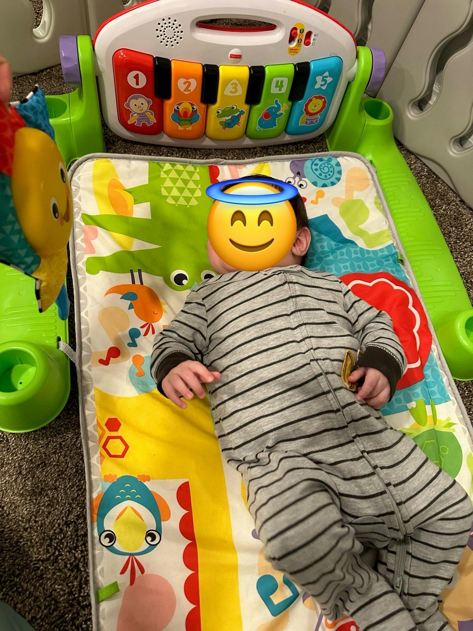Child lying on a playmat with a toy piano overhead