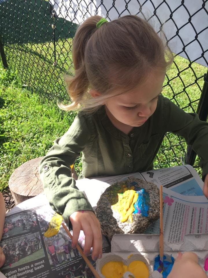 Child painting a rock outdoors