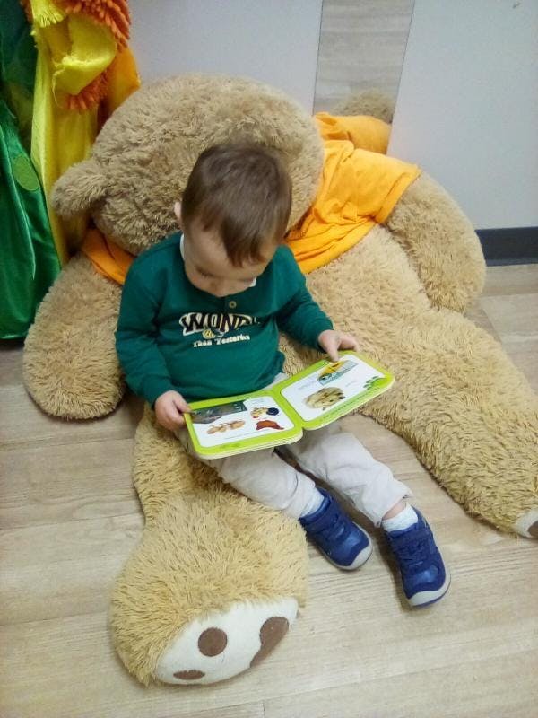 Child sitting on a large teddy bear and reading a book