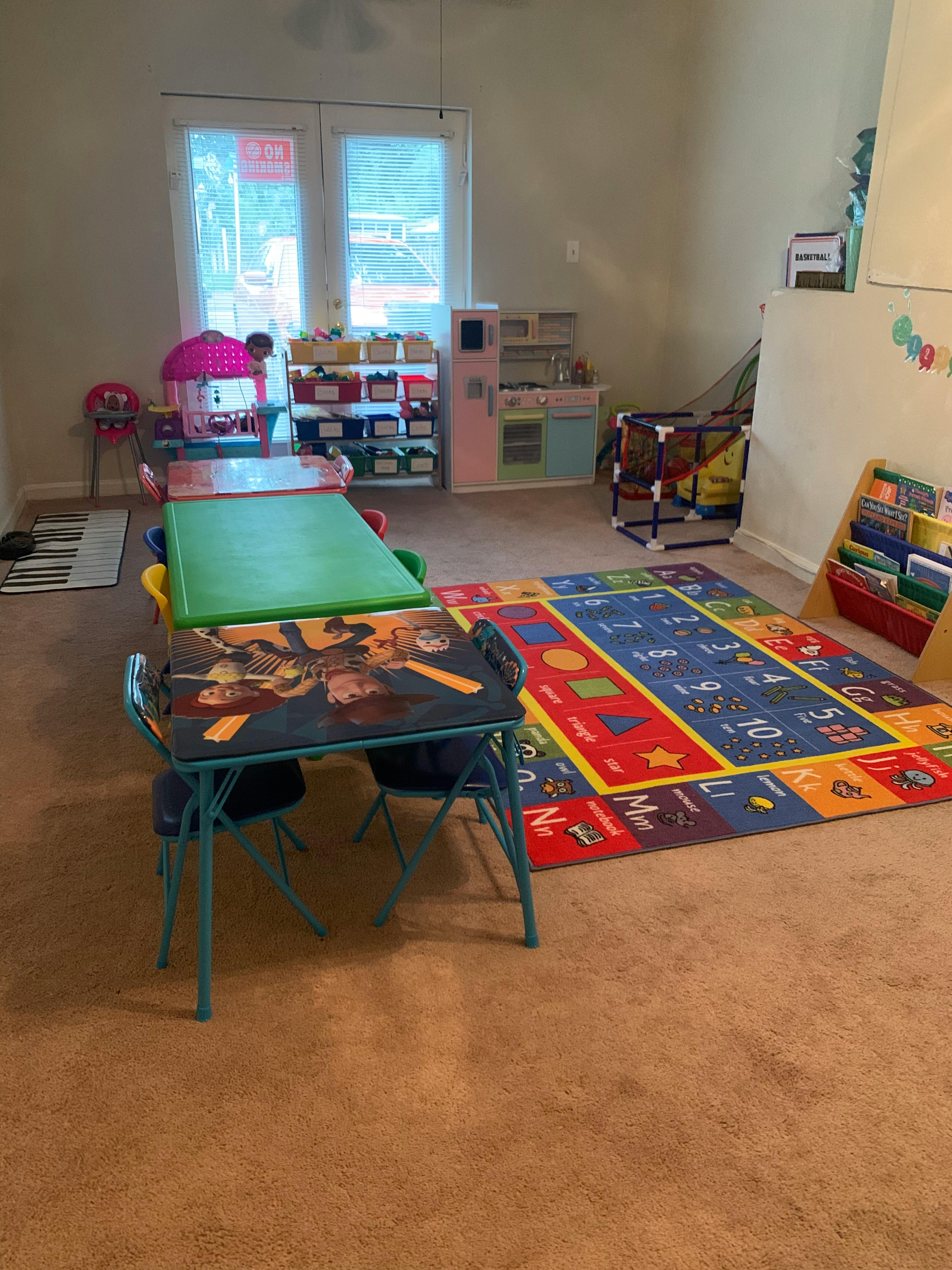 Children's play area with tables, chairs, and a colorful alphabet rug