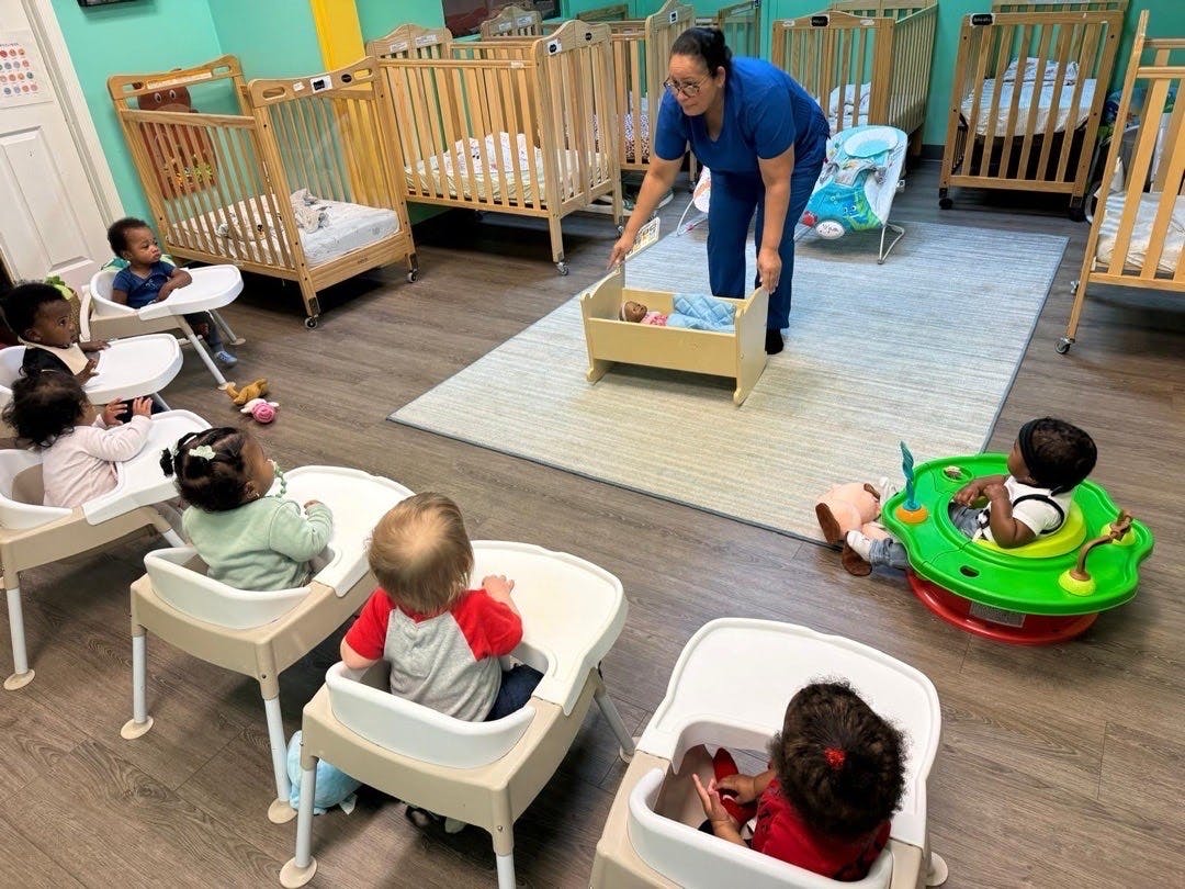 Adult demonstrating a baby doll to multiple children seated in high chairs