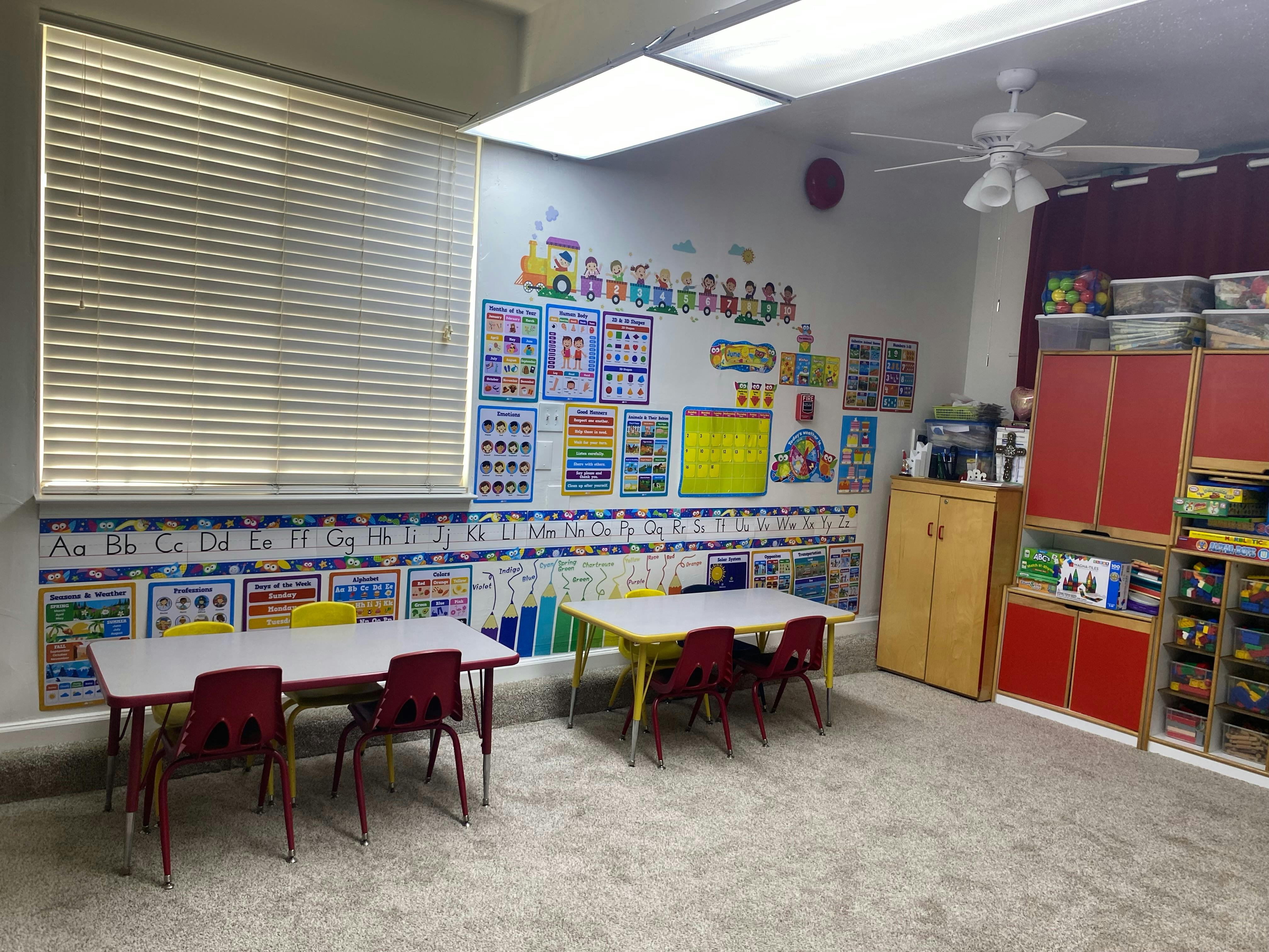 Classroom with small tables and chairs, educational posters on the wall