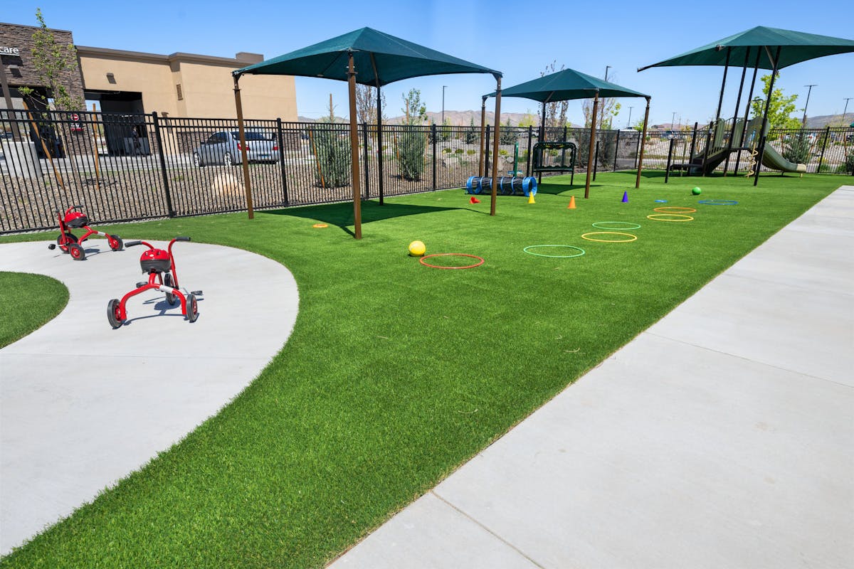 Outdoor playground with artificial turf, tricycles, and activity equipment