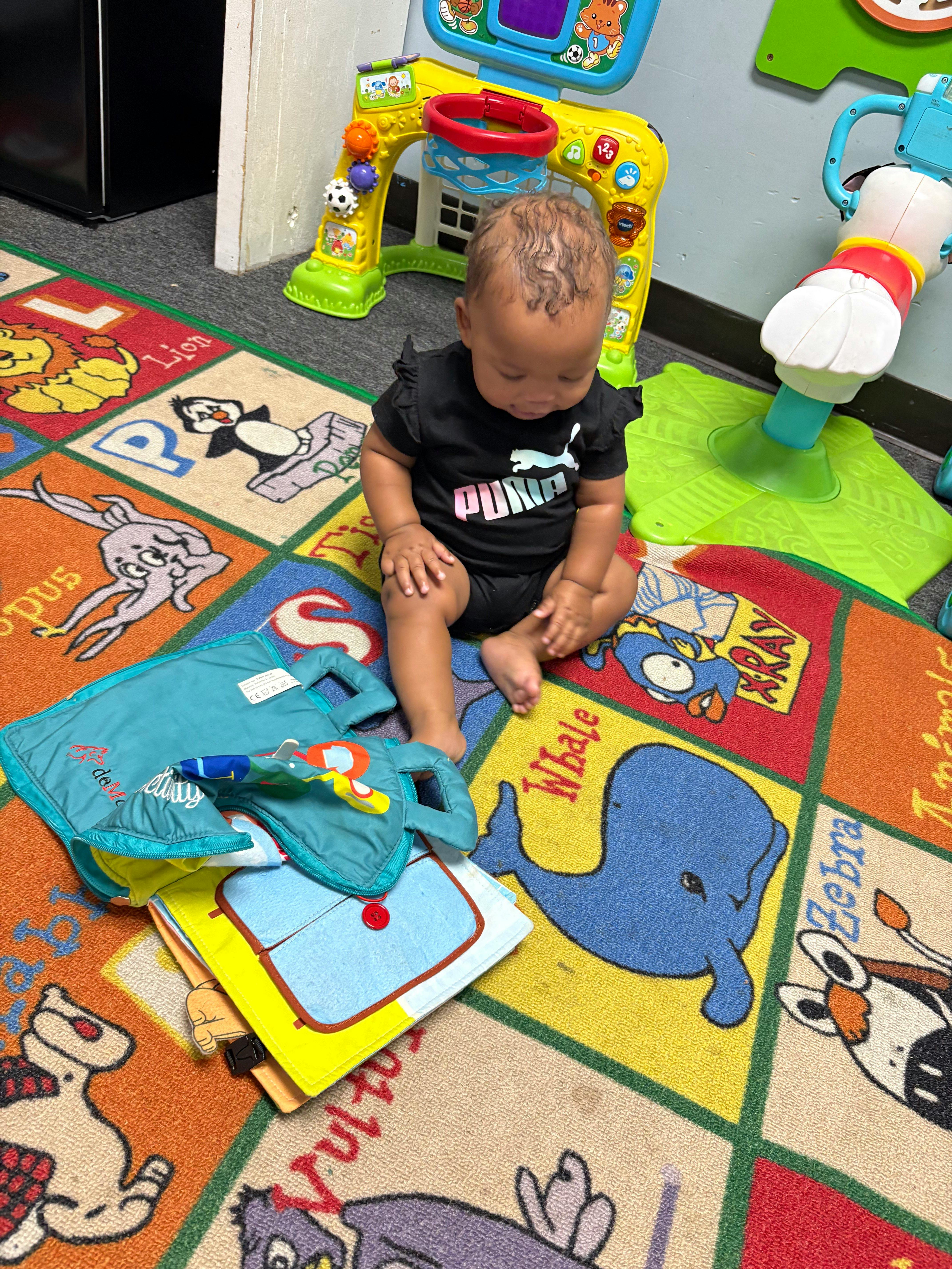 Baby sitting on a colorful alphabet rug, looking at soft activity books