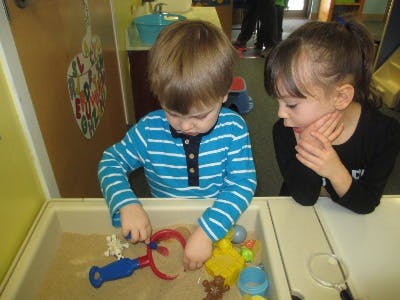 Two children playing with sand and toys in a sand table