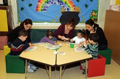 Three adults and four children at a table in a classroom