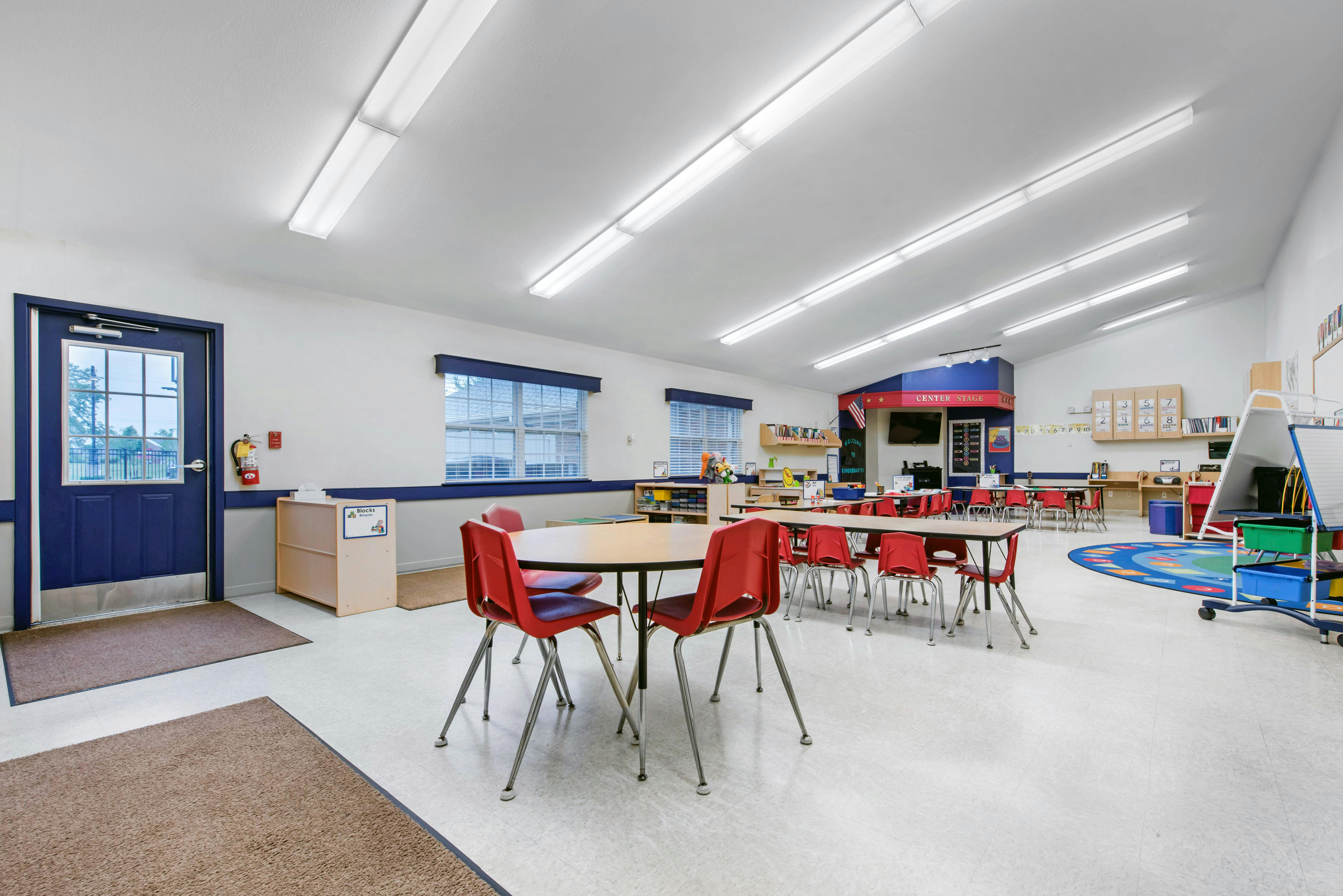 Empty classroom with small tables and red chairs, blue door on the left