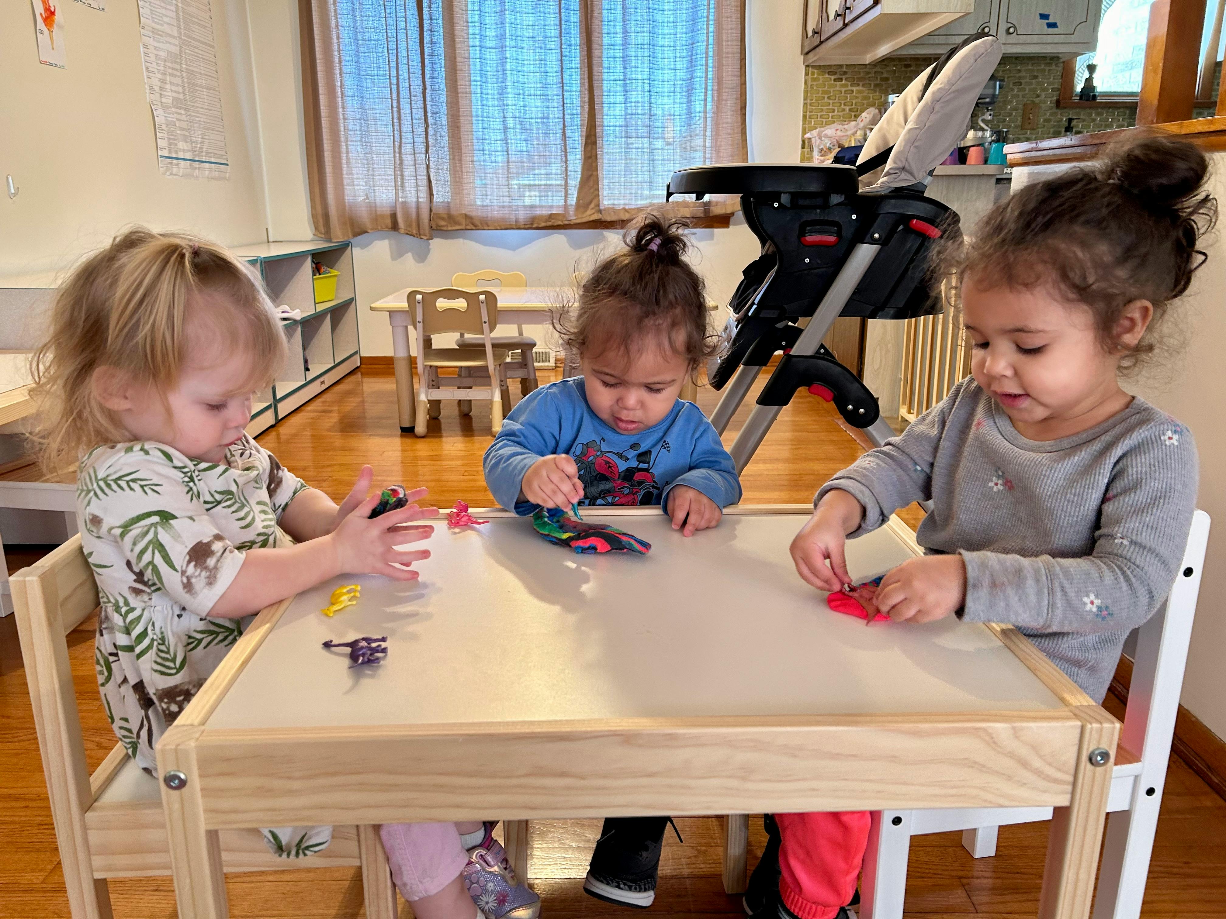 Three children playing with small objects at a table in a classroom