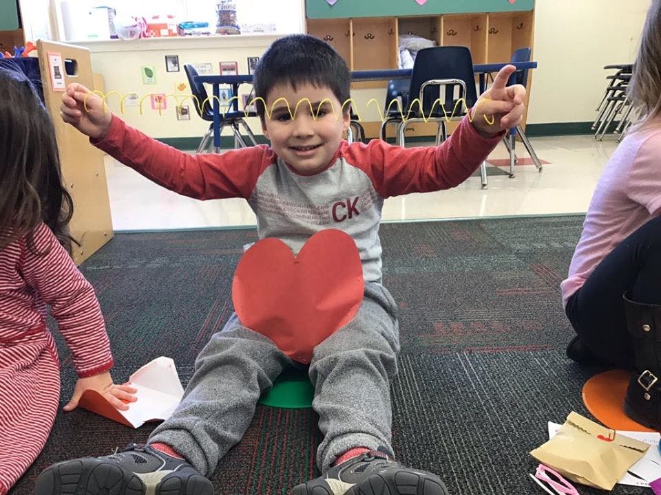 Child sitting on floor with red heart cutout, arms outstretched