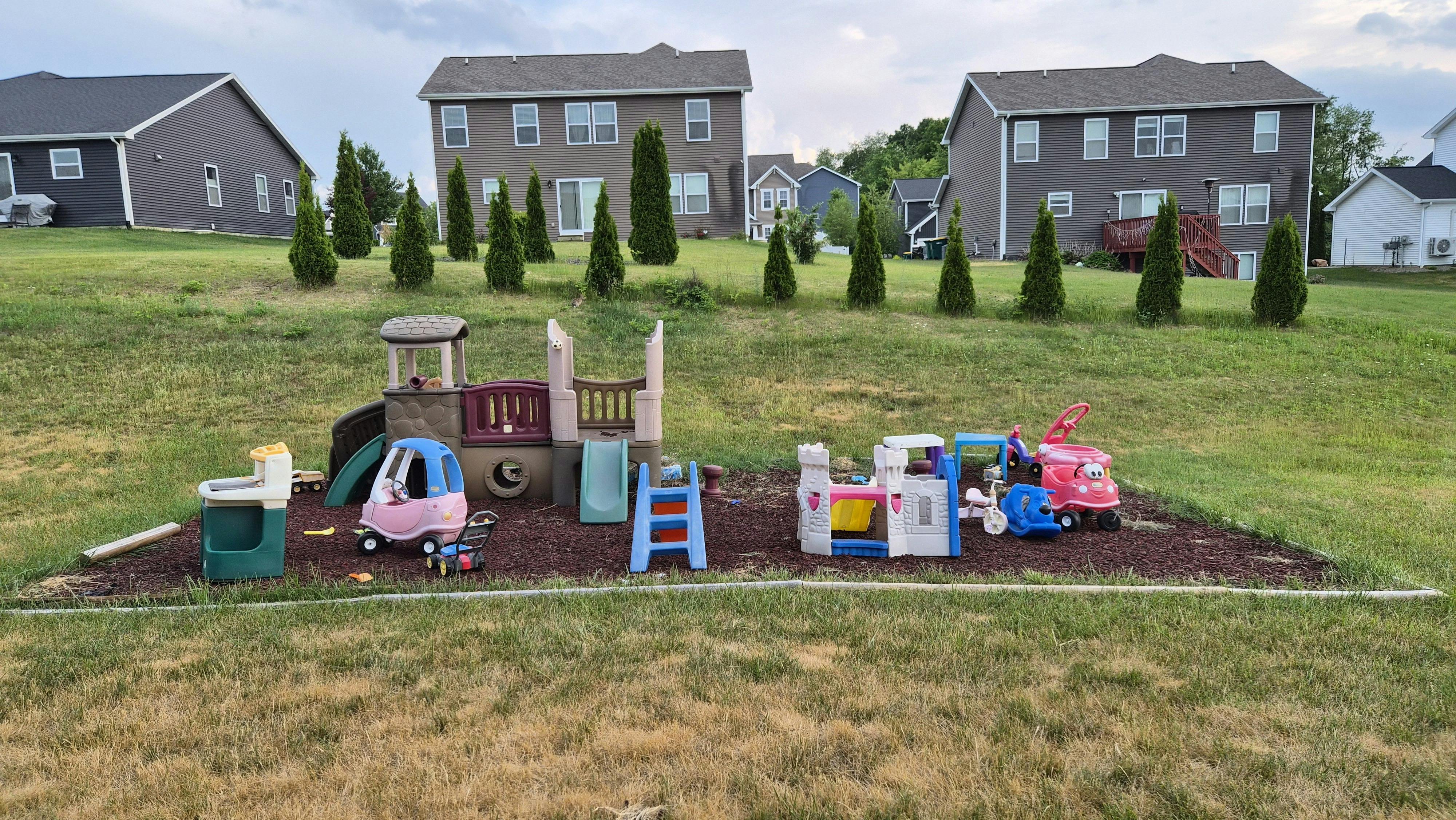 Plastic playground equipment and toy cars in a grassy residential backyard