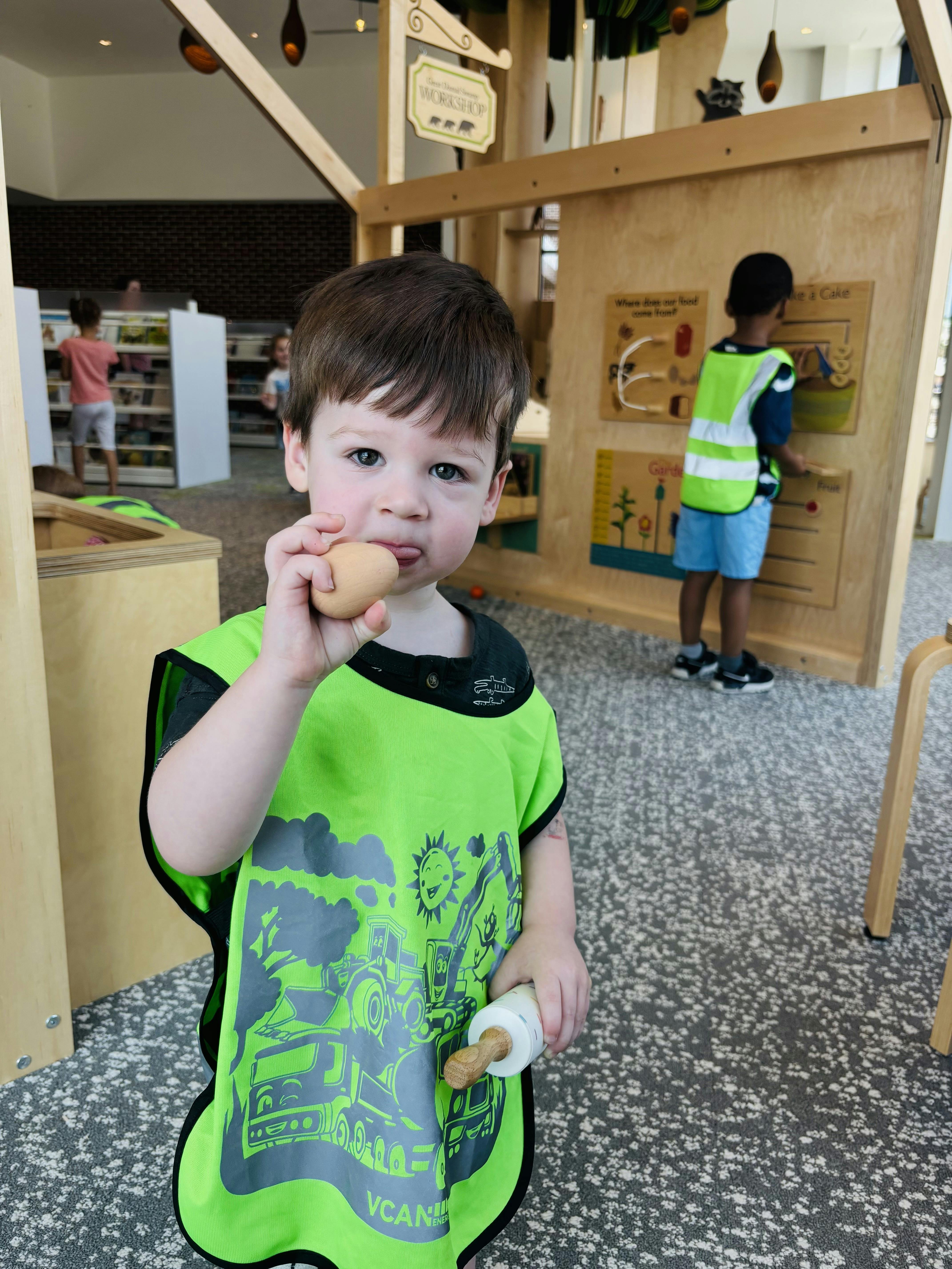 Child wearing a bright green vest holding a wooden play egg