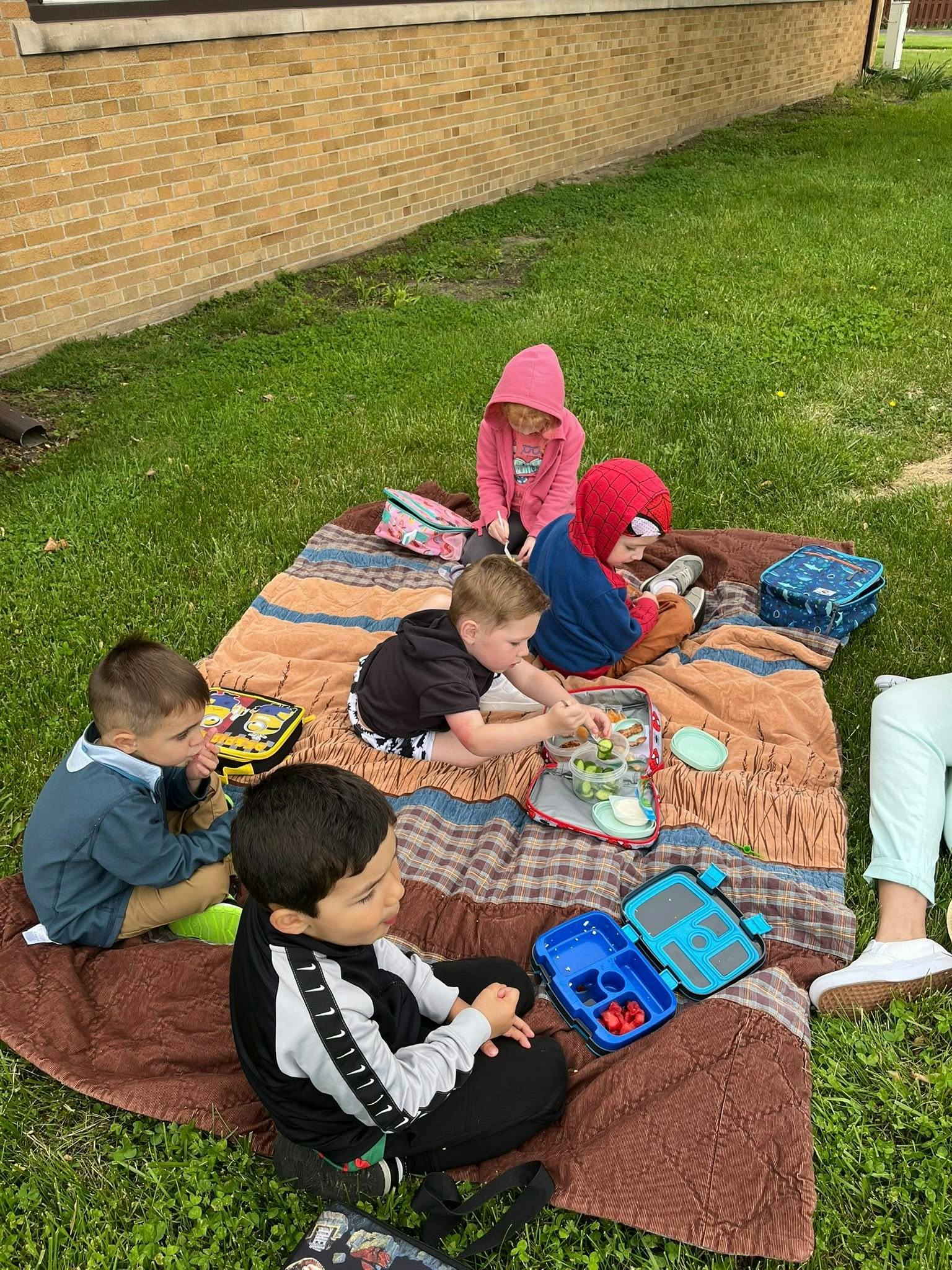 Children sitting on a blanket on grass, eating lunch