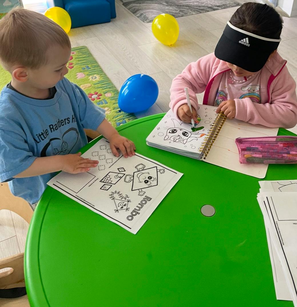 Two children coloring at a green table